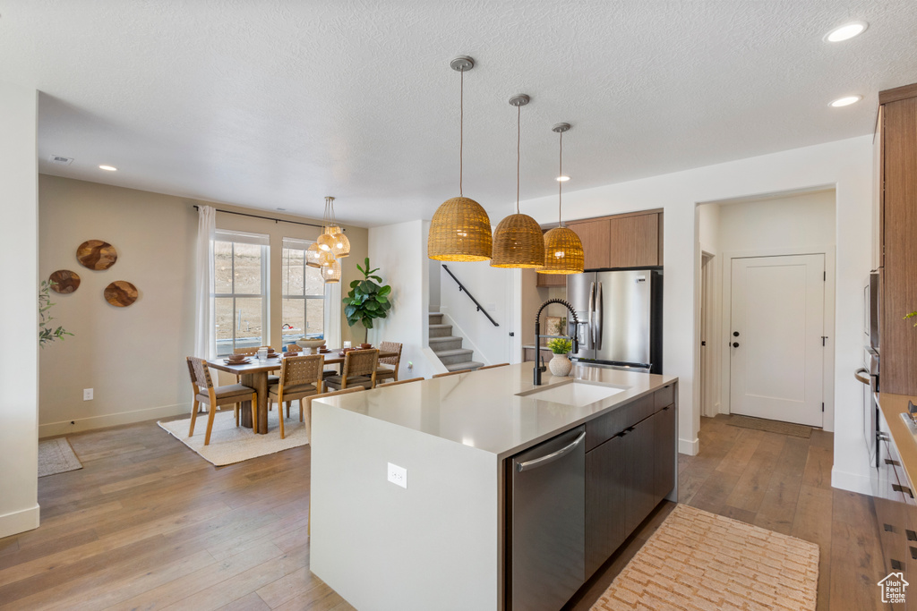 Kitchen with appliances with stainless steel finishes, recessed lighting, light wood-type flooring, light countertops, and a kitchen island with sink