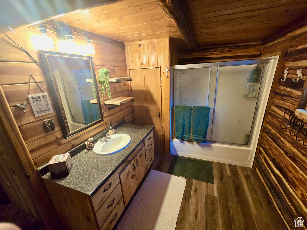 Bathroom with wooden ceiling, wood walls, wood finished floors, vanity, and combined bath / shower with glass door