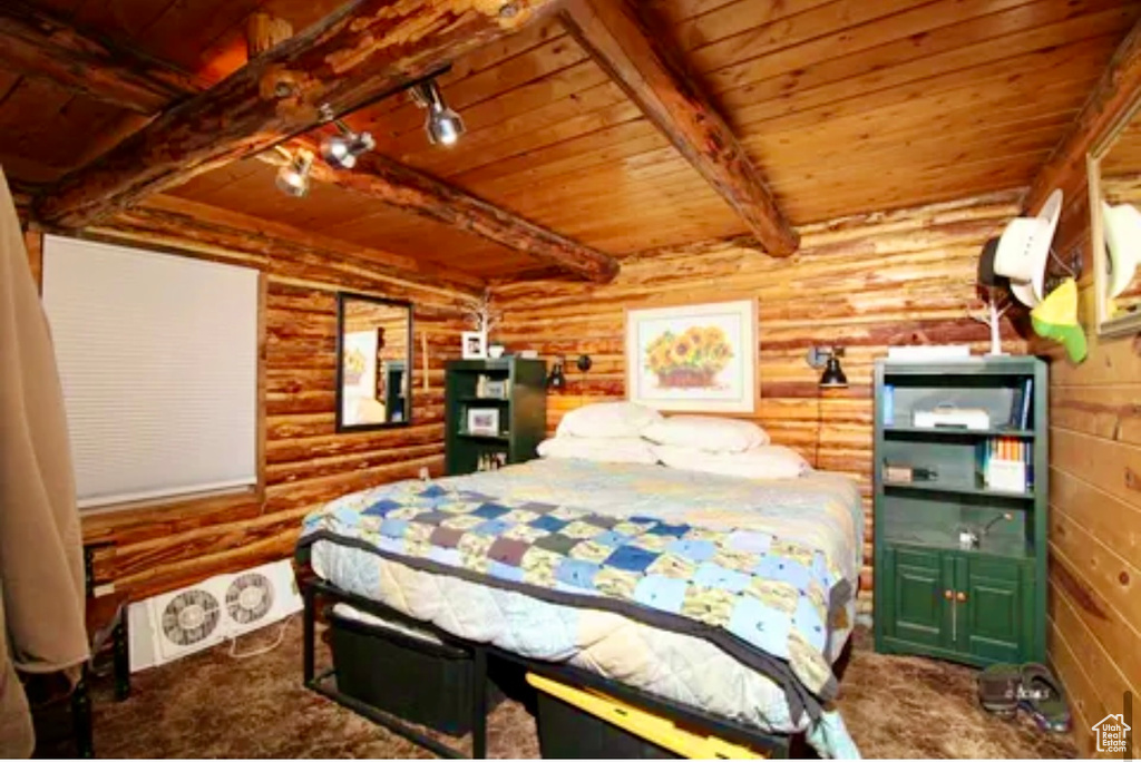 Carpeted bedroom with a wood ceiling with exposed beams, rustic walls, and track lighting