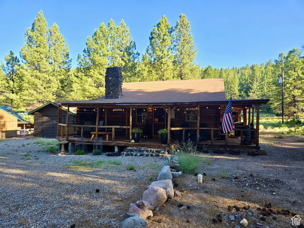 Rear view of house featuring covered porch, a chimney, and a wooded view