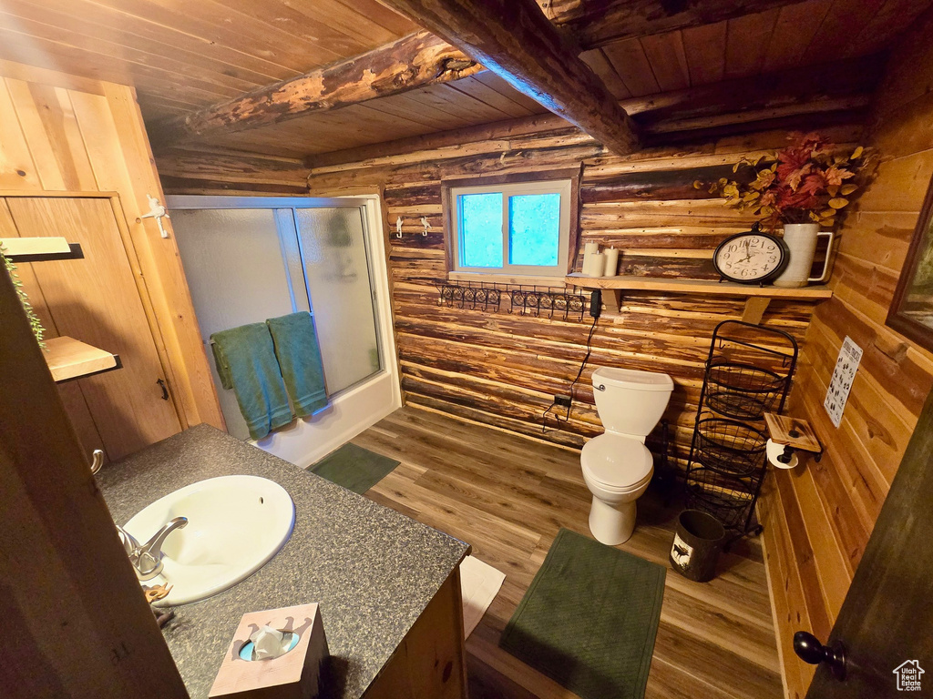 Full bathroom featuring a wooden ceiling with exposed beams, log walls, wood finished floors, vanity, and bath / shower combo with glass door