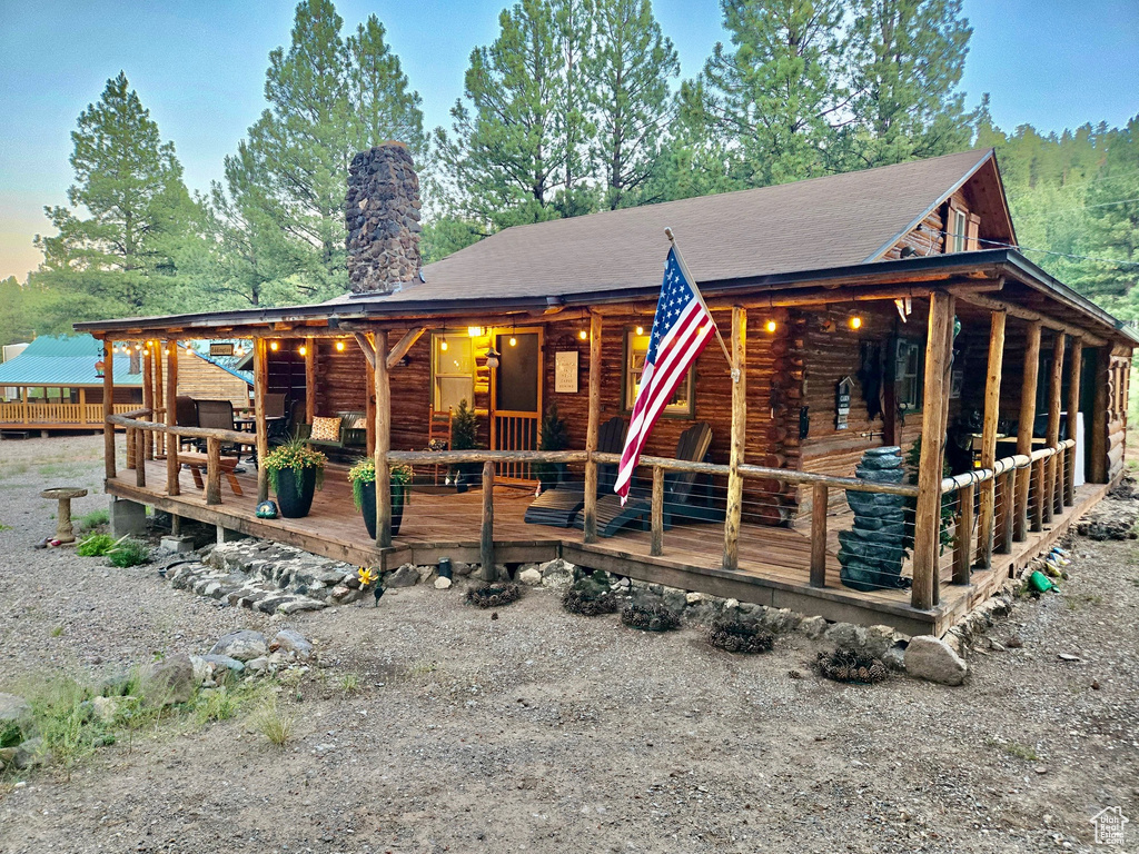 Log home featuring log exterior, a chimney, a shingled roof, and a deck