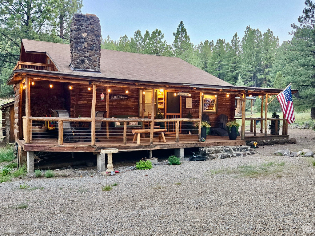 View of front of property featuring a chimney, covered porch, log exterior, and a shingled roof