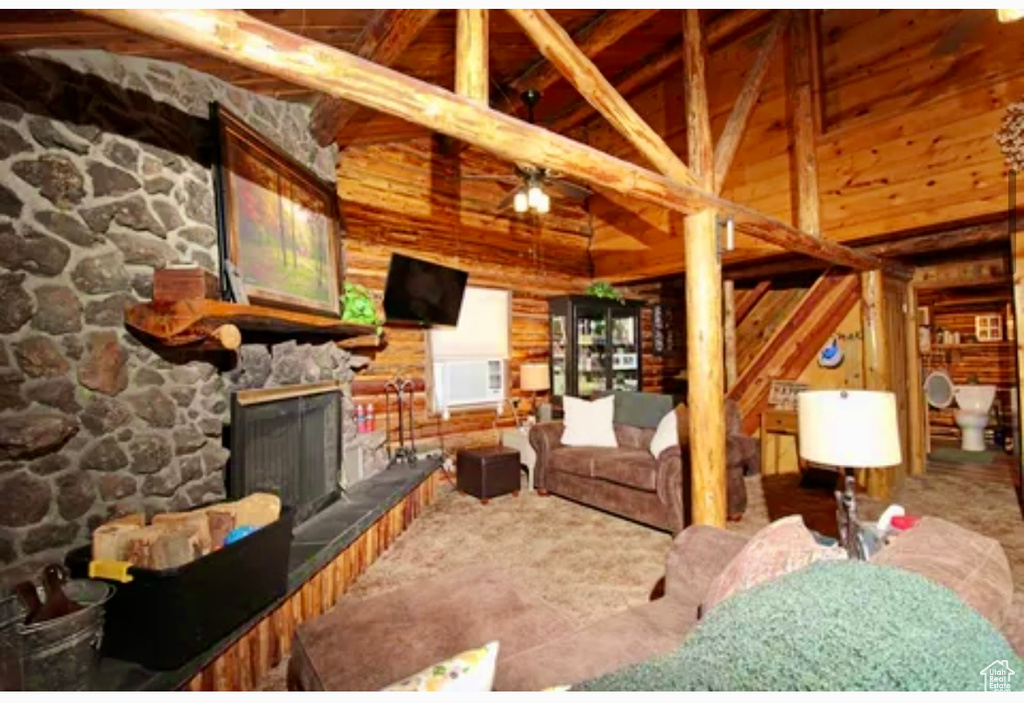 Living area featuring a fireplace, wooden walls, ceiling fan, high vaulted ceiling, and beam ceiling
