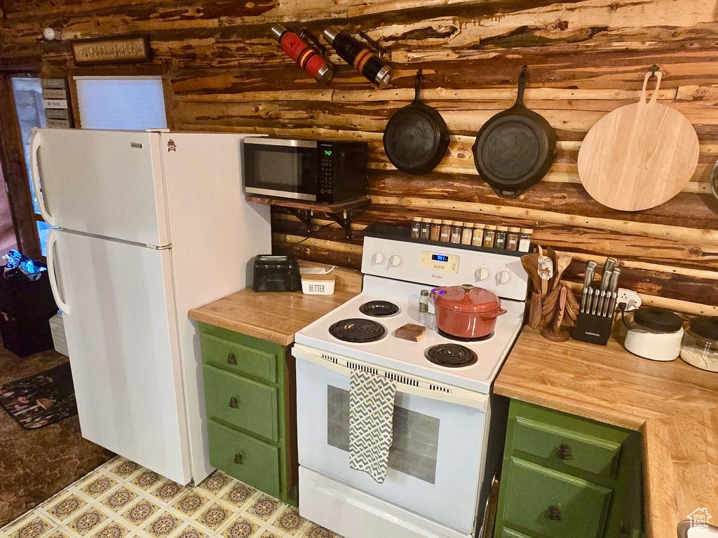 Kitchen with white appliances, log walls, green cabinetry, and butcher block counters