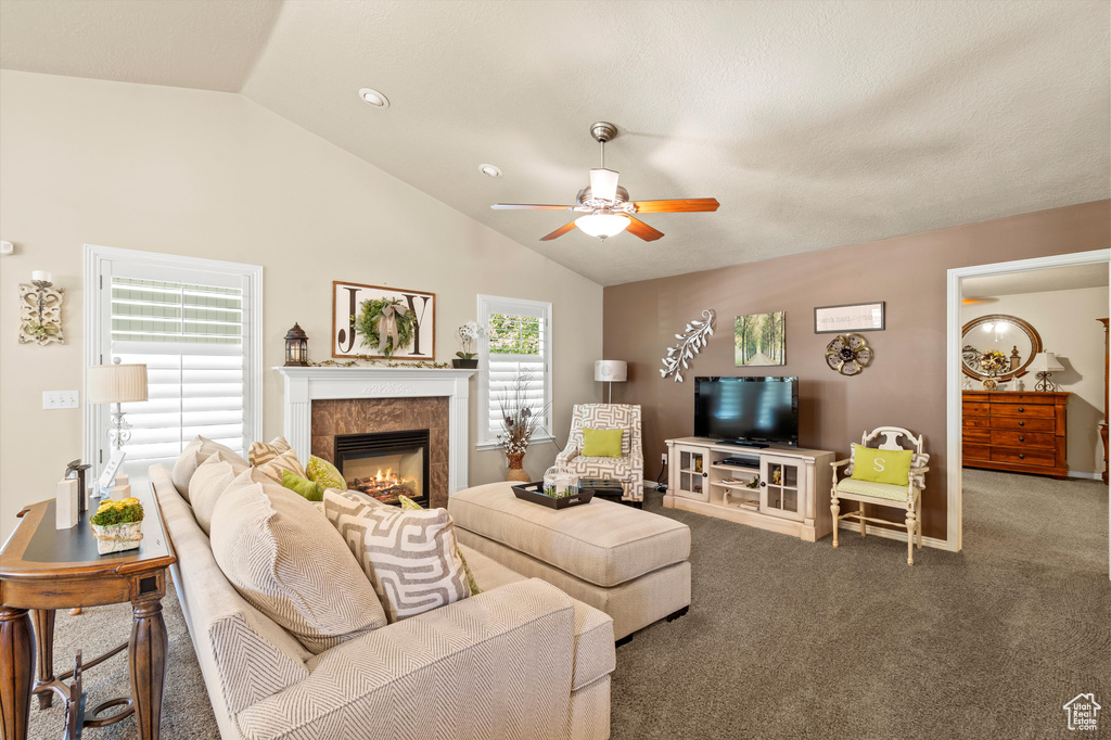 Carpeted living room featuring vaulted ceiling, ceiling fan, and a tile fireplace