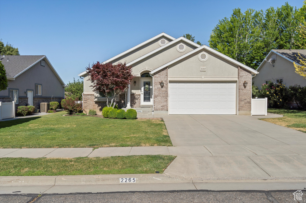 View of front of home with an attached garage, concrete driveway, a front lawn, and brick siding