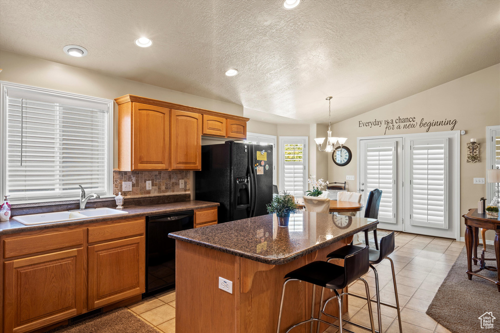 Kitchen featuring black appliances, a kitchen breakfast bar, a kitchen island, lofted ceiling, and a chandelier