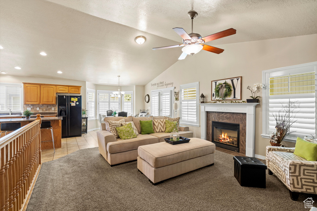 Living area with a ceiling fan, a tile fireplace, recessed lighting, vaulted ceiling, and a chandelier