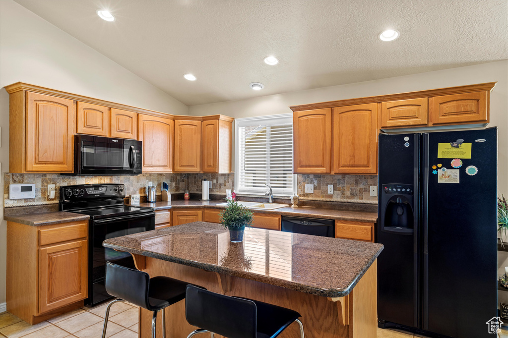 Kitchen featuring black appliances, lofted ceiling, a kitchen island, backsplash, and a breakfast bar