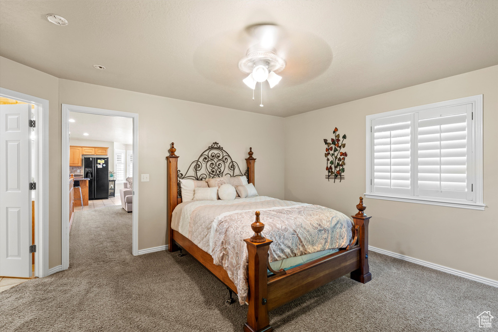 Bedroom with black refrigerator with ice dispenser, light colored carpet, recessed lighting, and ceiling fan