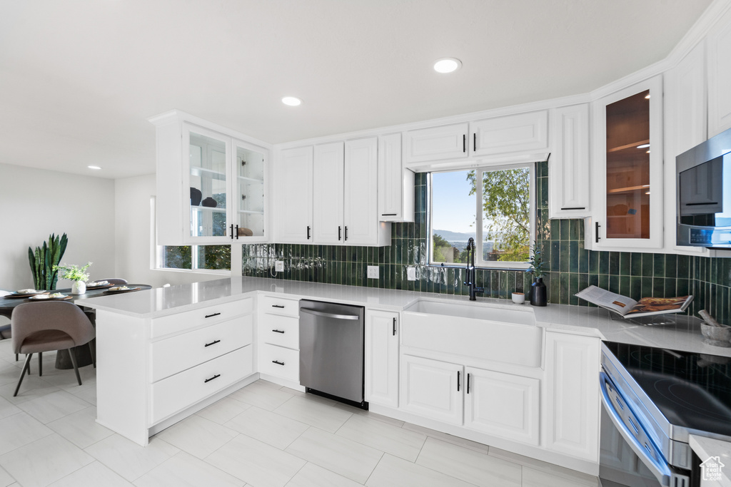 Kitchen featuring stainless steel appliances, a peninsula, decorative backsplash, white cabinets, and recessed lighting