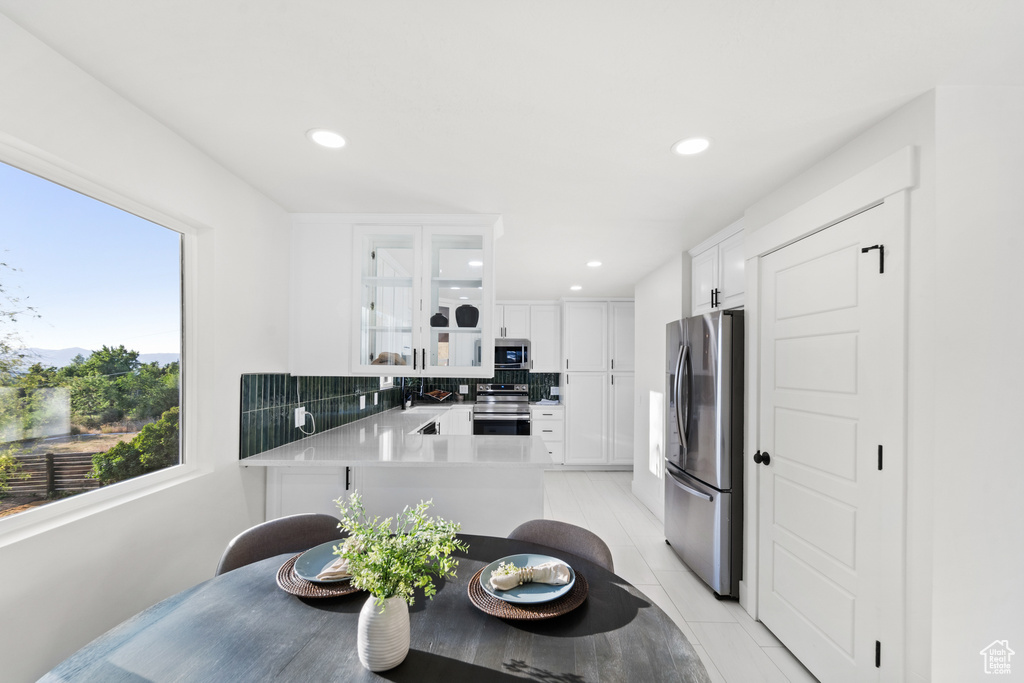 Kitchen featuring stainless steel appliances, glass insert cabinets, backsplash, white cabinets, and light countertops
