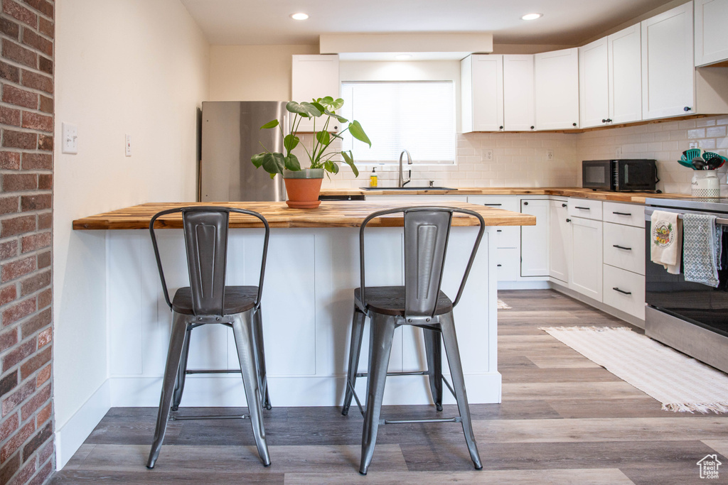 Kitchen featuring butcher block counters, stainless steel appliances, a kitchen breakfast bar, recessed lighting, and brick wall