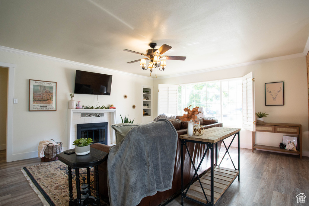 Living area with ornamental molding, a glass covered fireplace, a ceiling fan, and wood finished floors