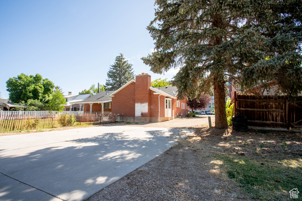 View of side of property with a chimney, brick siding, driveway, and roof with shingles