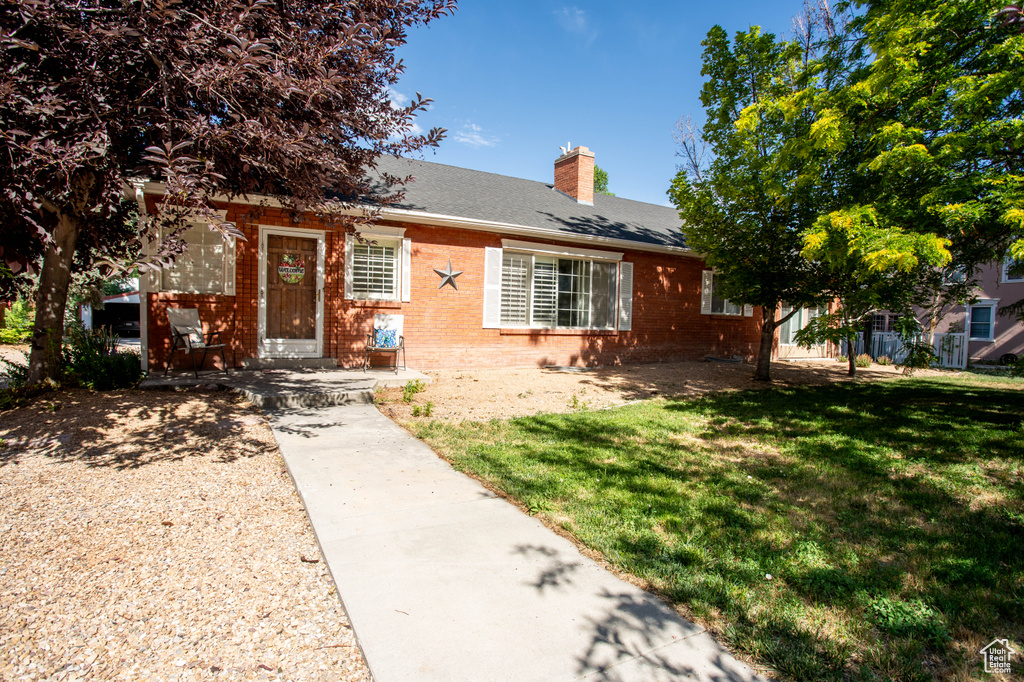 View of front facade featuring brick siding, a chimney, a front yard, and a shingled roof