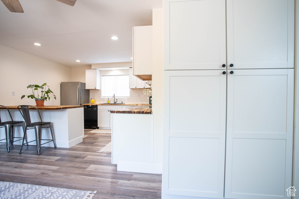 Kitchen featuring freestanding refrigerator, black dishwasher, white cabinetry, light wood-style floors, and a breakfast bar area