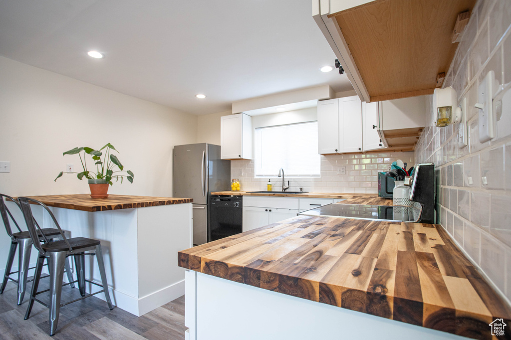 Kitchen with wood counters, black dishwasher, freestanding refrigerator, a kitchen breakfast bar, and wood finished floors