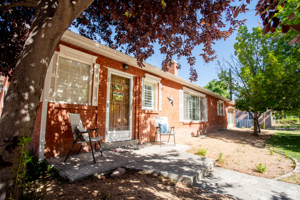 View of front facade featuring a chimney, brick siding, and a patio