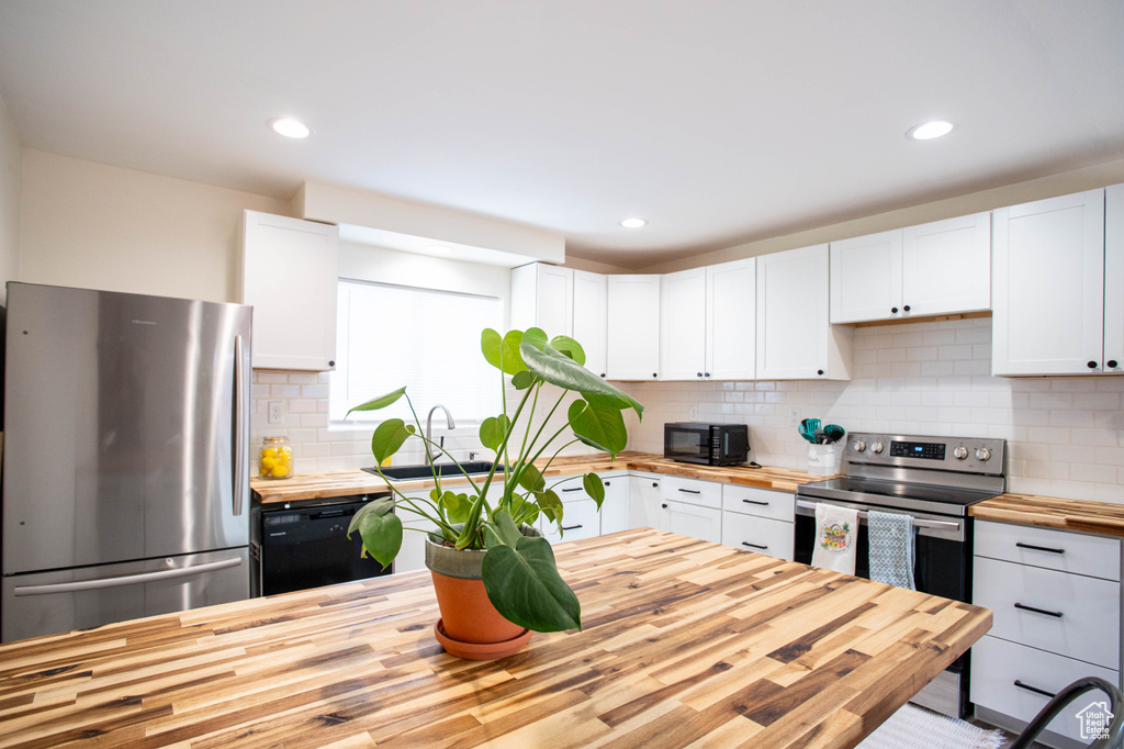 Kitchen with wood counters, black appliances, white cabinetry, backsplash, and recessed lighting