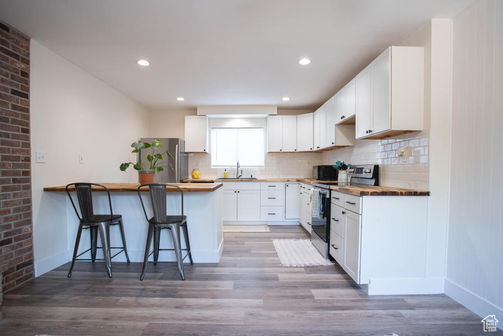 Kitchen with butcher block counters, appliances with stainless steel finishes, a peninsula, a breakfast bar area, and recessed lighting