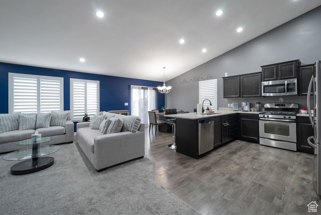 Kitchen with stainless steel appliances, a peninsula, a chandelier, open floor plan, and lofted ceiling