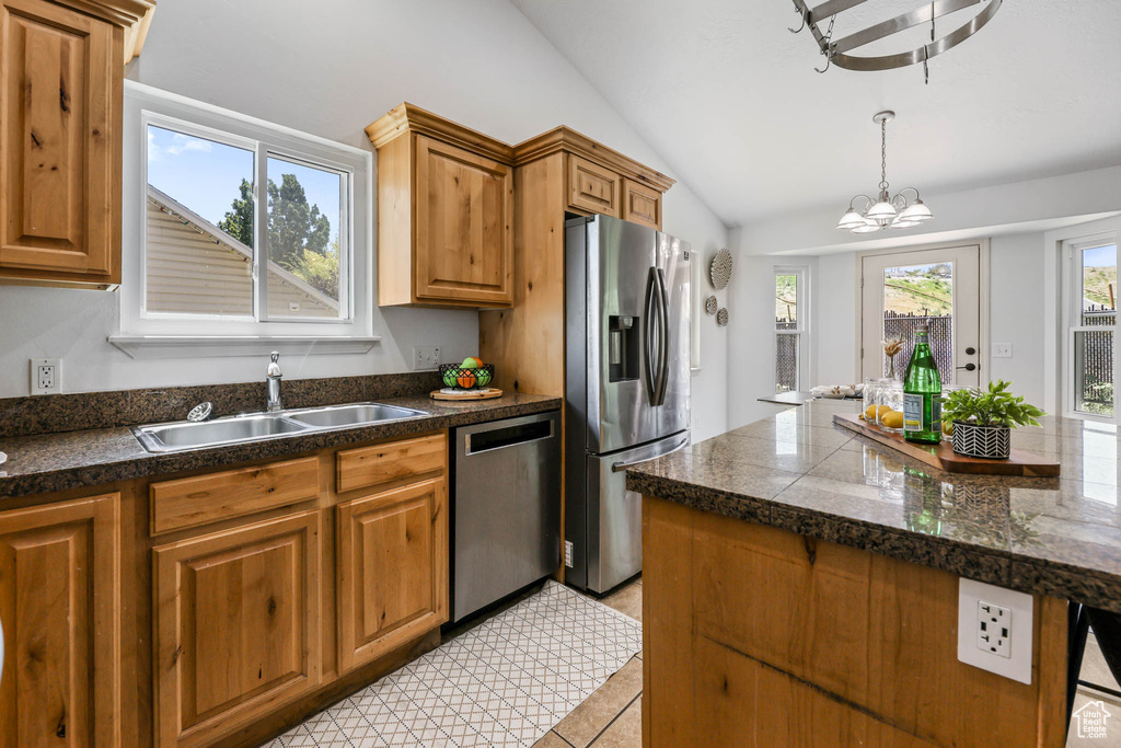 Kitchen featuring appliances with stainless steel finishes, tile counters, vaulted ceiling, a chandelier, and brown cabinetry