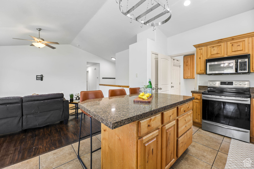Kitchen with stainless steel appliances, tile countertops, a kitchen breakfast bar, lofted ceiling, and light tile patterned floors
