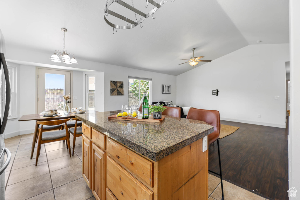 Kitchen featuring vaulted ceiling, a center island, a breakfast bar, ceiling fan, and a chandelier