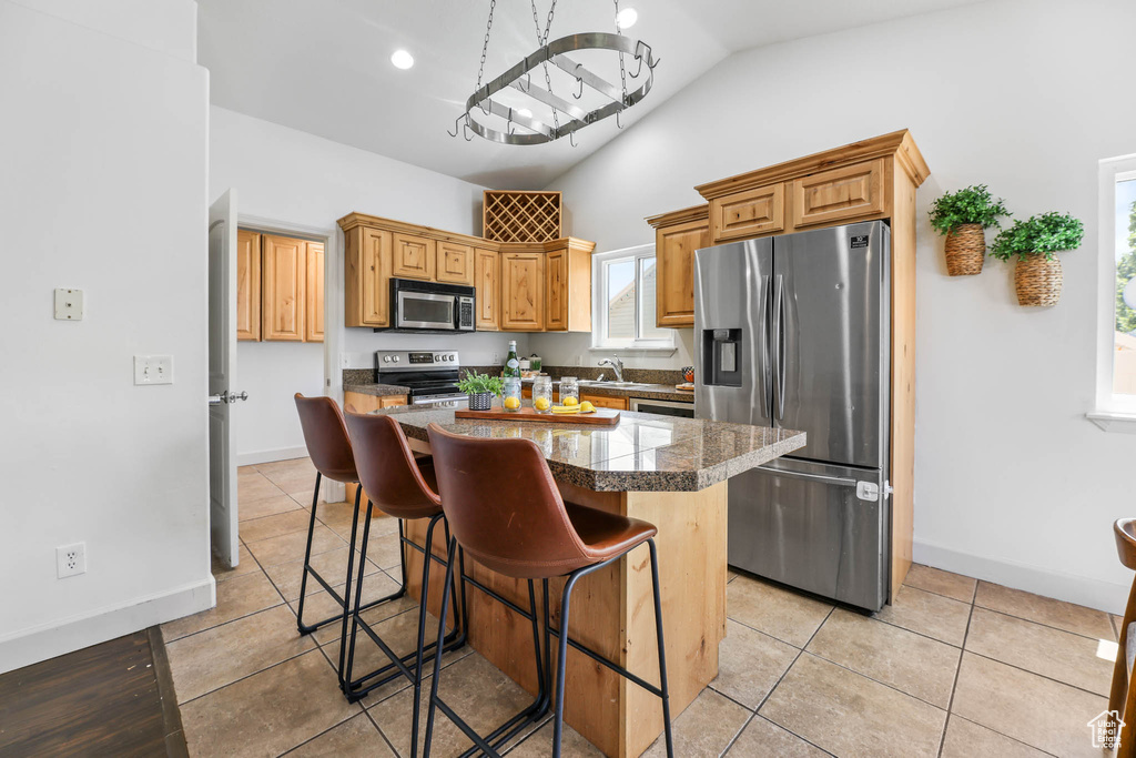 Kitchen with appliances with stainless steel finishes, vaulted ceiling, a chandelier, a kitchen bar, and a center island