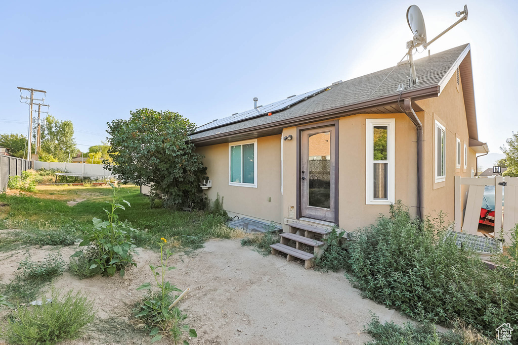 Back of house featuring entry steps, roof mounted solar panels, stucco siding, and roof with shingles
