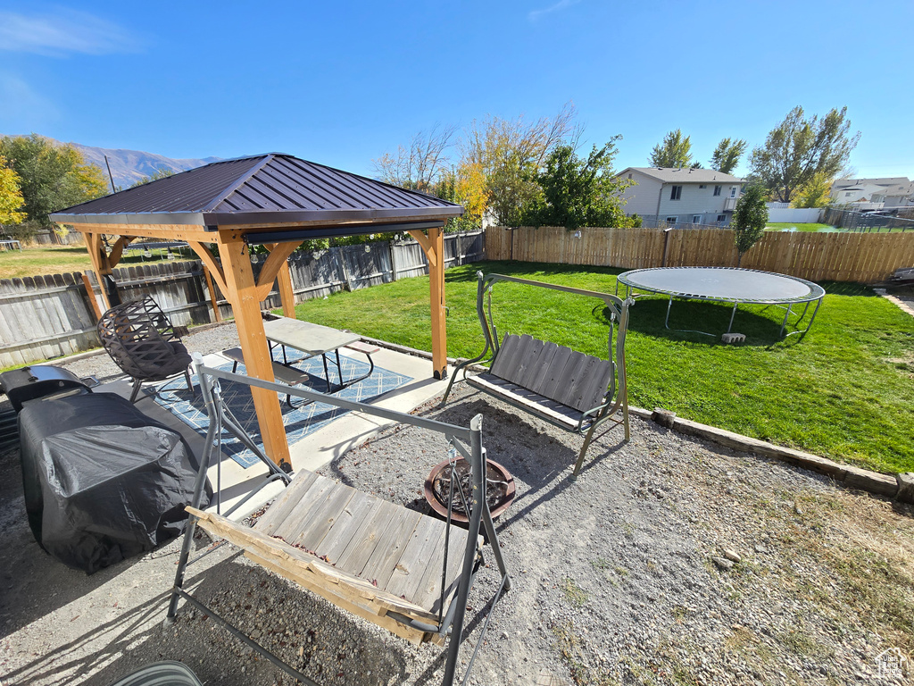 Fenced backyard featuring a trampoline and a gazebo