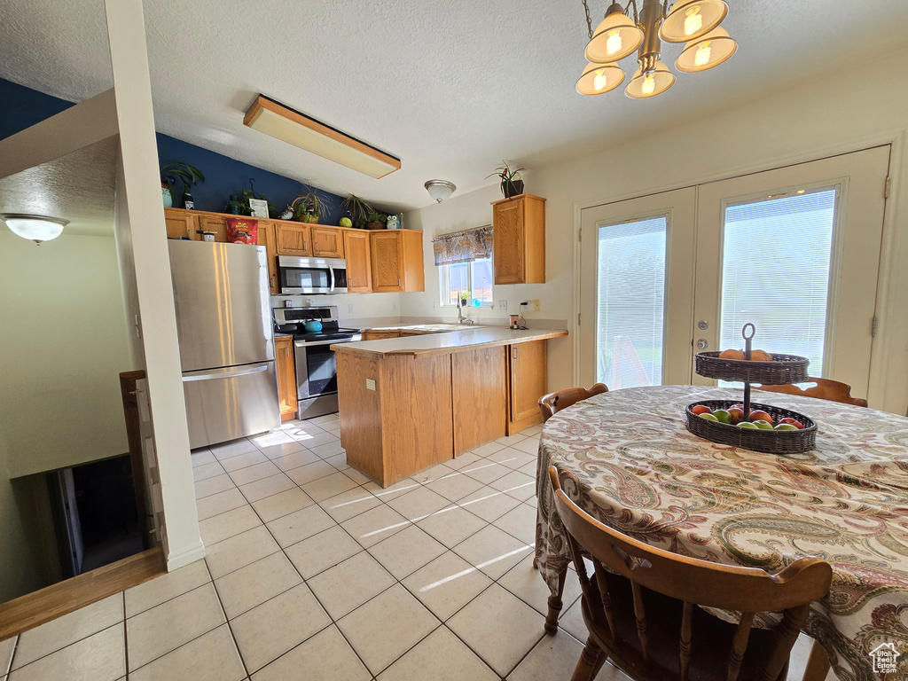 Kitchen with stainless steel appliances, a peninsula, light tile patterned floors, light countertops, and a chandelier