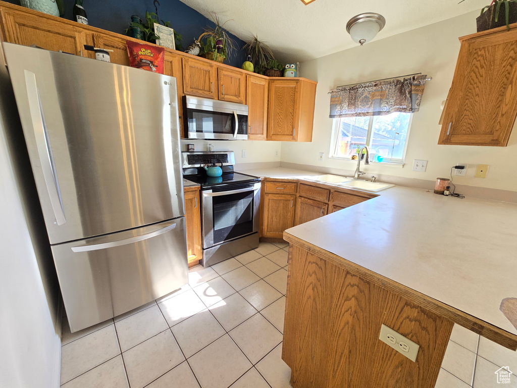 Kitchen featuring appliances with stainless steel finishes, light countertops, light tile patterned flooring, and brown cabinets