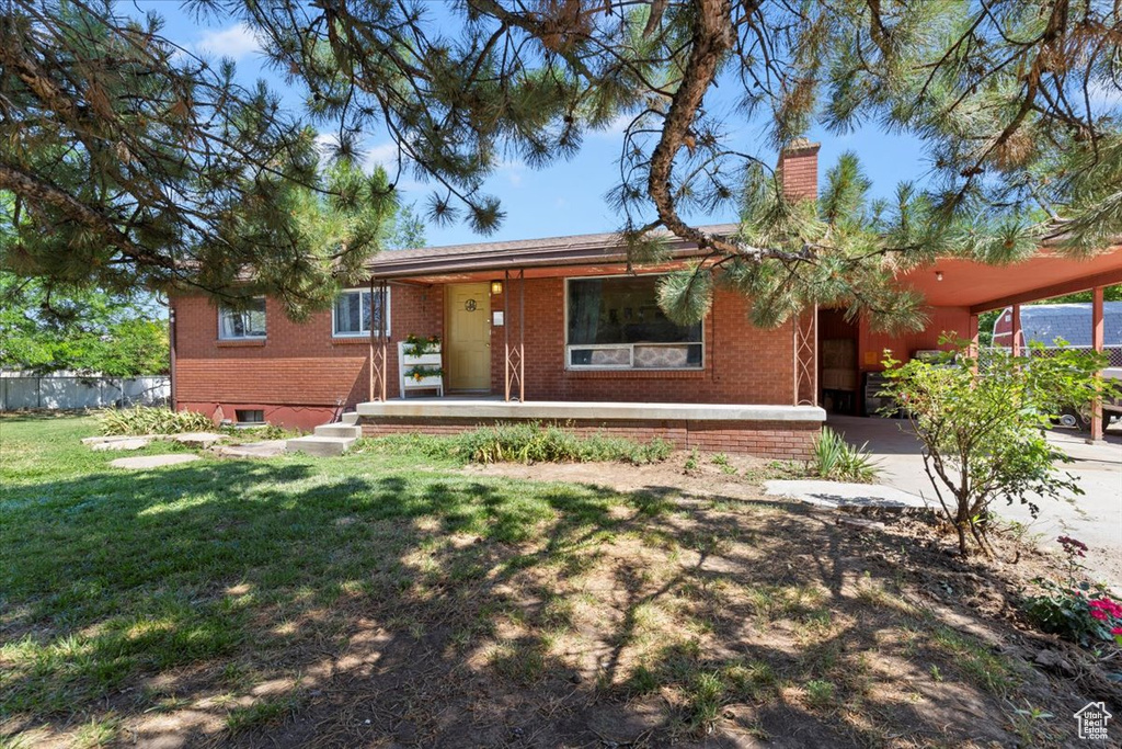 Ranch-style house featuring brick siding, a front yard, a chimney, a carport, and a porch