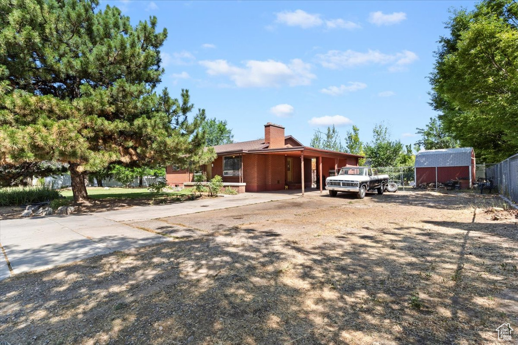 View of front of home featuring driveway, an attached carport, a chimney, and an outbuilding