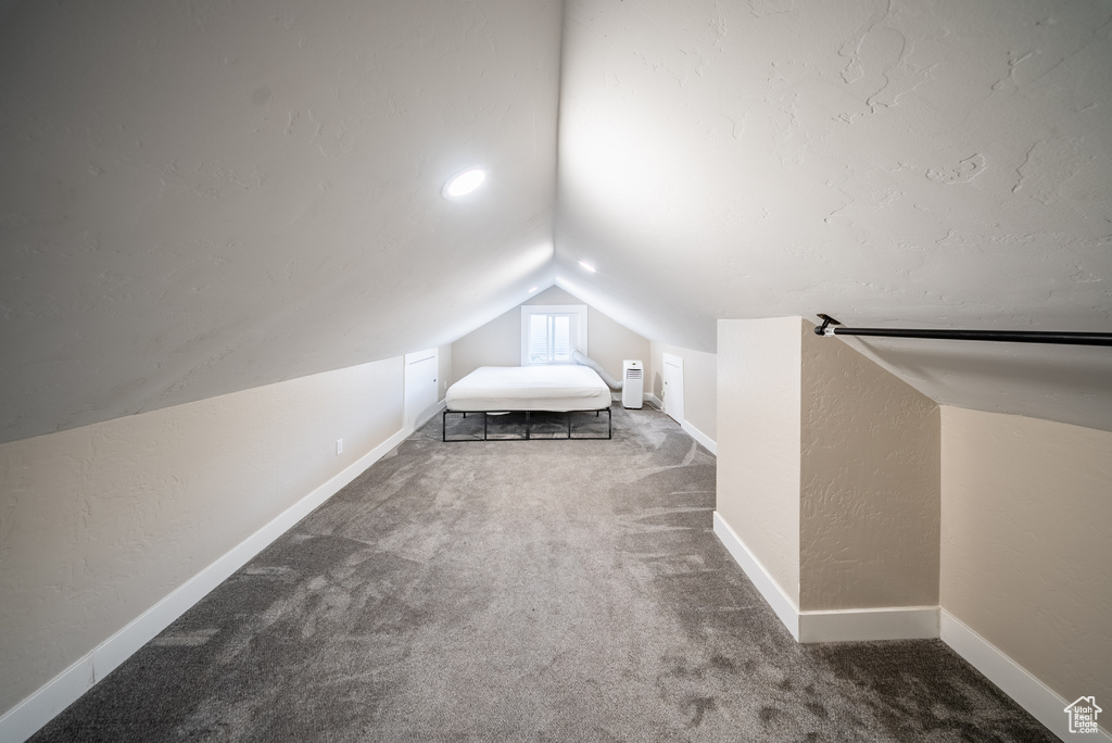 Bedroom featuring vaulted ceiling, carpet flooring, and a textured wall