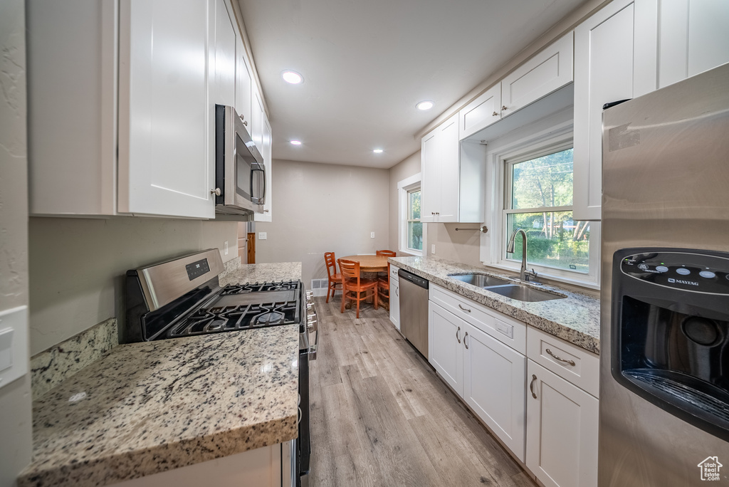 Kitchen with stainless steel appliances, light wood-type flooring, white cabinetry, recessed lighting, and light stone countertops