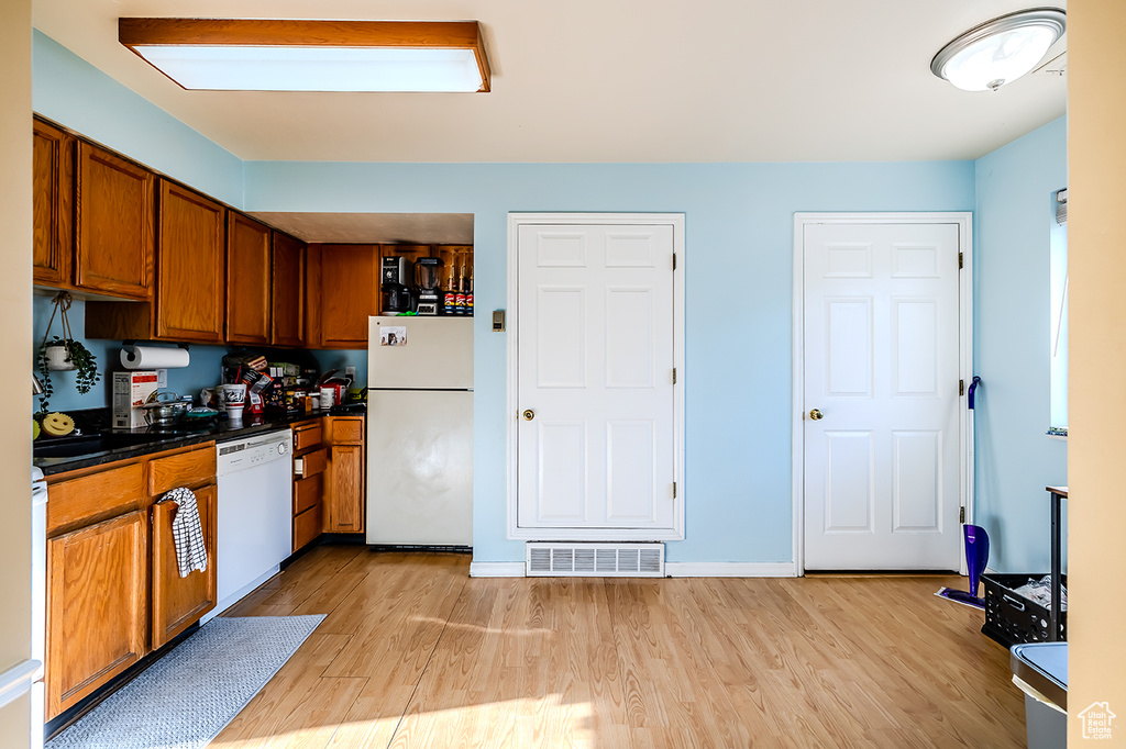 Kitchen featuring white appliances, brown cabinets, light wood-style floors, and dark countertops