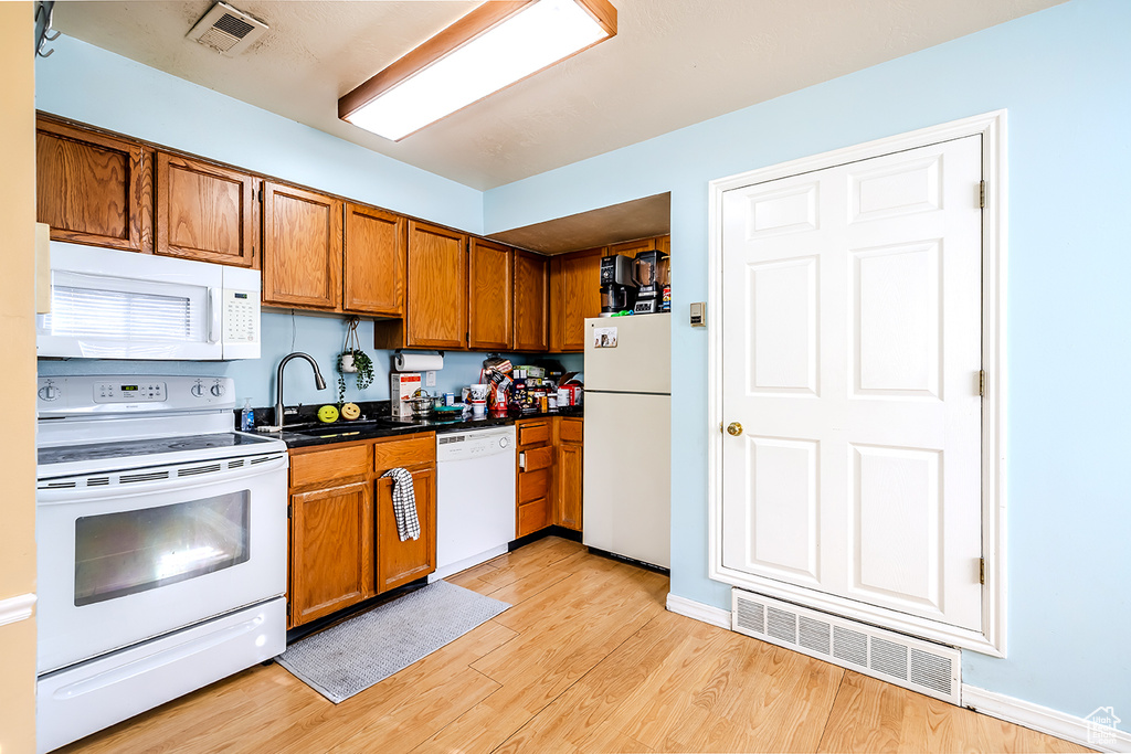 Kitchen featuring white appliances, brown cabinets, dark countertops, and light wood-style floors
