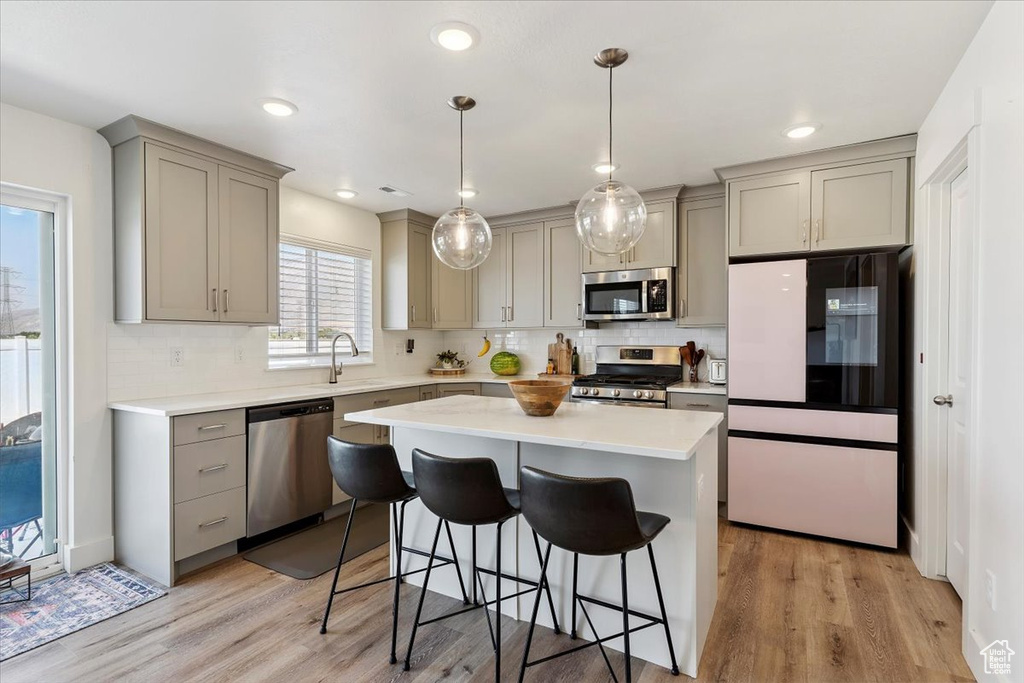 Kitchen featuring appliances with stainless steel finishes, gray cabinetry, a breakfast bar area, backsplash, and recessed lighting