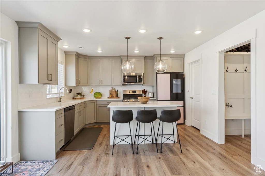 Kitchen with stainless steel appliances, gray cabinetry, a kitchen breakfast bar, light wood-style flooring, and recessed lighting