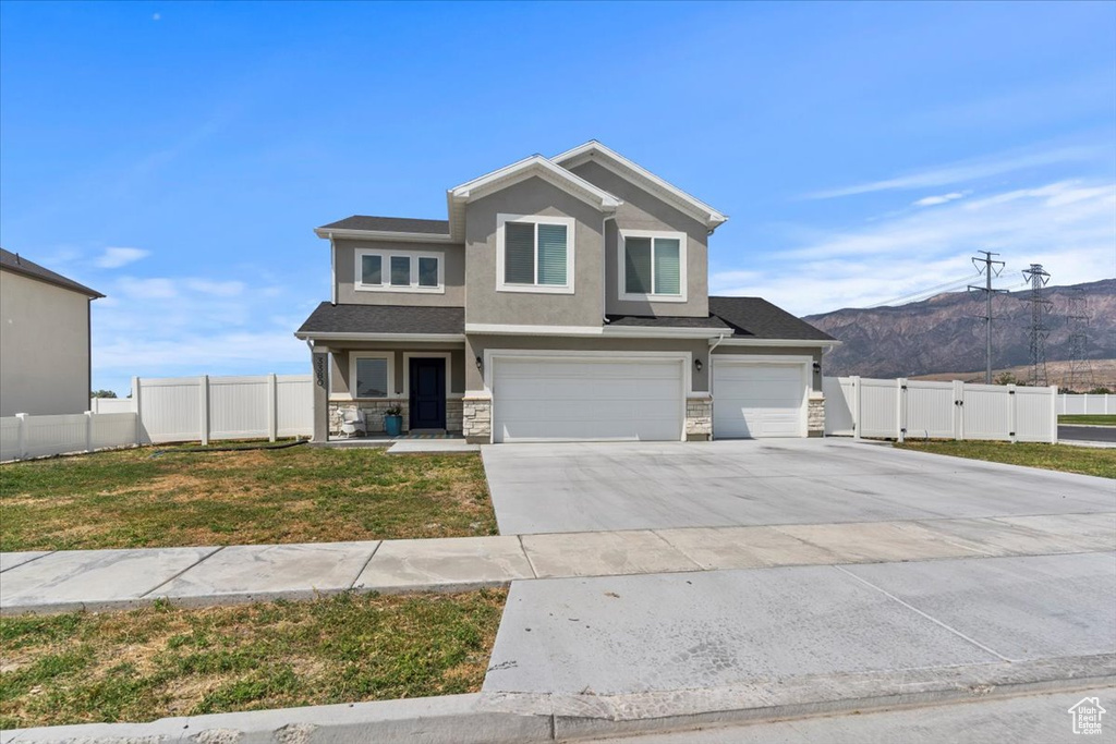 View of front of home featuring a mountain view, an attached garage, stucco siding, stone siding, and driveway