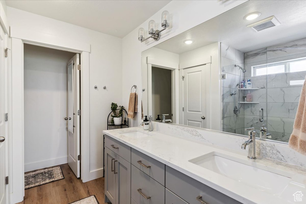 Bathroom with double vanity, a marble finish shower, wood finished floors, and recessed lighting
