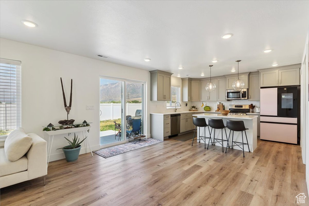 Kitchen featuring appliances with stainless steel finishes, gray cabinets, a breakfast bar area, light countertops, and light wood-type flooring