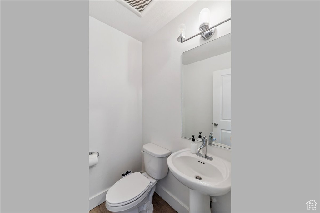Half bathroom featuring wood finished floors and toilet