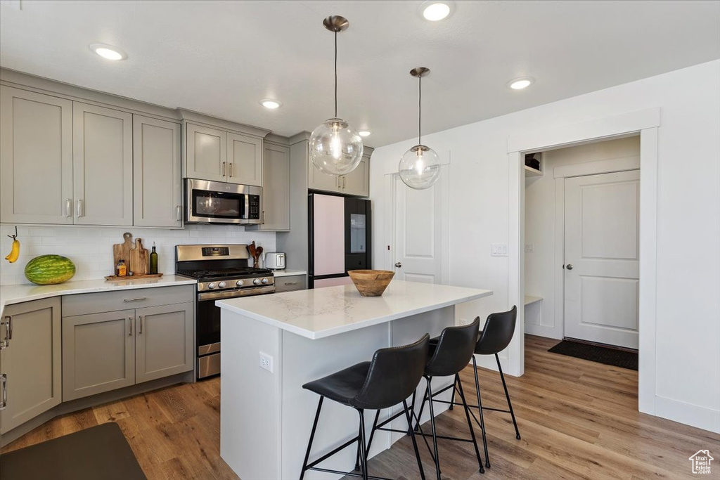 Kitchen featuring stainless steel appliances, gray cabinets, light wood finished floors, a breakfast bar area, and decorative backsplash