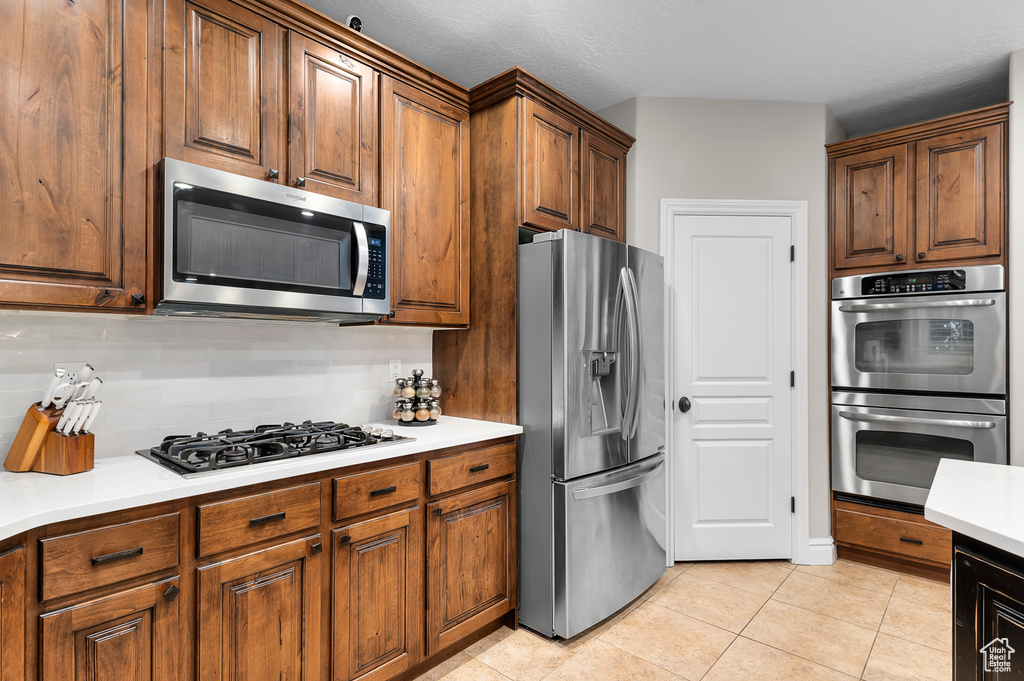 Kitchen with appliances with stainless steel finishes, light tile patterned floors, light countertops, backsplash, and brown cabinetry