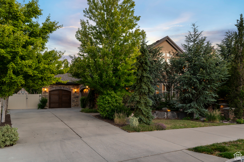 View of property hidden behind natural elements featuring a gate, driveway, stone siding, and a garage